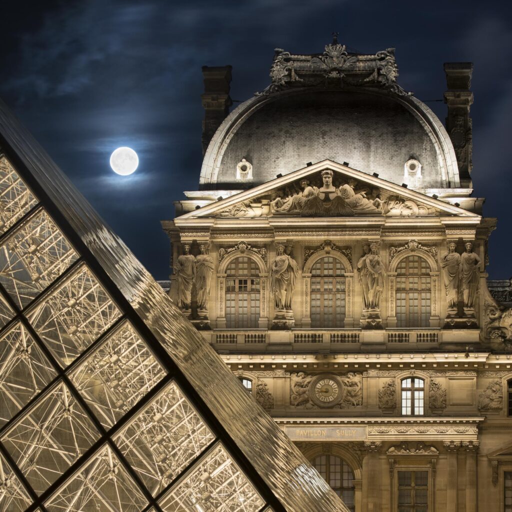 Photographie de nuit avec sur 3 plans la pyramide, le musée du Louvre et la lune