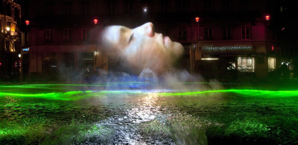 Éclairage festif à Lyon lors de la Fête des Lumières: projection d'un visage en hologramme au-dessus de l'eau